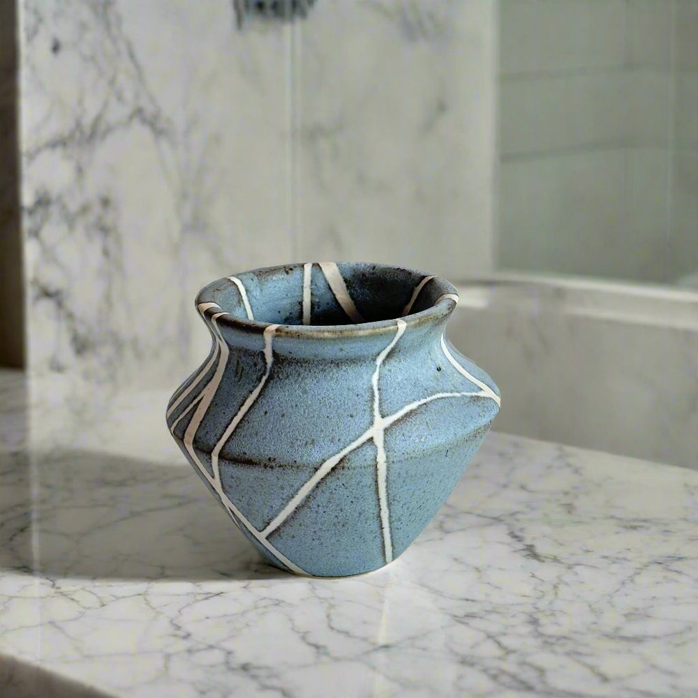 Medium sized vase with white lines in random patter against a matte light blue background. 