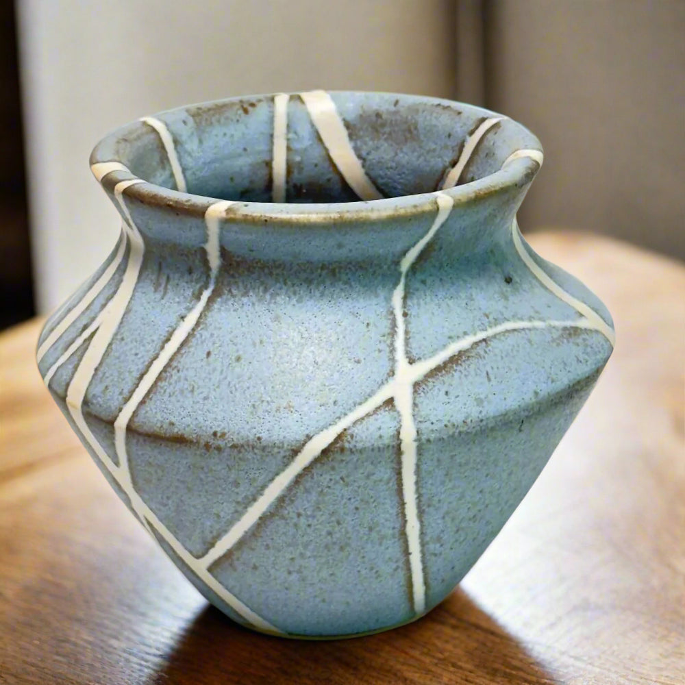 
                      
                        Close up Medium sized vase with white lines in random patter against a matte light blue background. 
                      
                    
